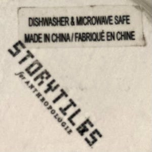 Puede incluir: Primer plano de una etiqueta blanca con texto negro. La etiqueta dice "Dishwasher & Microwave Safe" y "Made in China / Fabriqu&eacute; en Chine". Debajo, la palabra "Storytiles" est&aacute; impresa diagonalmente en negro, con "for Anthropologie" debajo.