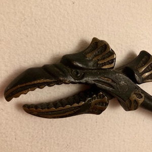 May include: A vintage bronze nutcracker shaped like a dragon's head with a detailed design and gold accents.