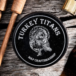 May include: A black round container with the words "TURKEY TITANS" and "M&P CRAFTSMANSHIP" in white lettering. A stylized image of a turkey is in the center of the container.