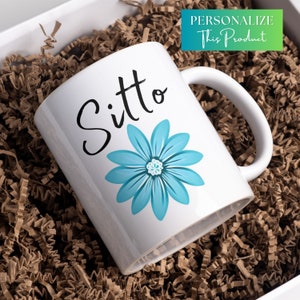 May include: White ceramic mug with a blue flower and the word "Sitto" in black lettering.