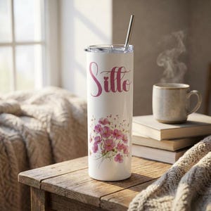 May include: A white insulated tumbler with a floral design and the name "Sitto" in pink script. The tumbler has a silver straw and a lid. A bouquet of pink flowers is printed on the tumbler.