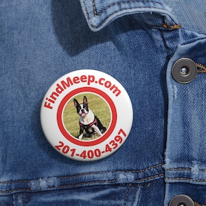 May include: A white button with a red border and text that reads "FindMeep.com" and "201-400-4397". The button features a photo of a Boston Terrier dog wearing a pink harness. The button is pinned to a denim jacket.