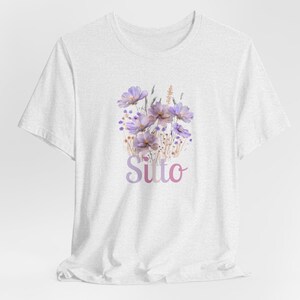 May include: White t-shirt with a watercolor design of purple flowers and the word "Sutto" in pink and purple lettering.