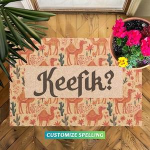 May include: A welcome mat with a camel pattern in shades of orange and brown. The mat has a white border and the text "Keefik?" in black. The mat is on a wooden floor.
