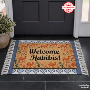 May include: A rectangular doormat with a camel and cactus pattern, and the words "Welcome Habibis!" in black. The doormat is layered on a blue and white patterned rug with fringe.