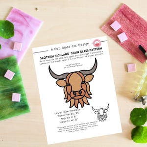 May include: A printed pattern for a Scottish Highland stain glass design. The design features a cartoon illustration of a Highland cow. The pattern is on a white paper with the text "Scottish Highland Stain Glass Pattern". The image includes pink and green glass pieces and a glass cutter.