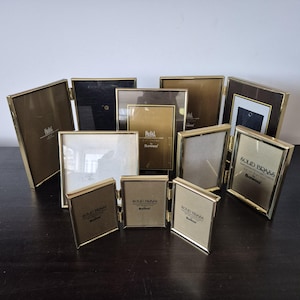 May include: A collection of gold-toned picture frames, some with a black backing, all with the text "Solid Brass" and "Bowen" on them.