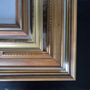 May include: A multi-layered picture frame featuring a combination of natural wood tones and metallic gold accents. The frame consists of several nested borders with varying textures, including smooth wood, beaded detailing, and polished gold trim.