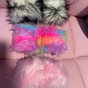 May include: A collection of four faux fur accessories. Two are black and white with long, shaggy fibers. One is a rectangular piece featuring a vibrant, multi-colored tie-dye pattern. The final piece is a solid, light pink faux fur item.