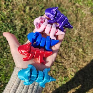 May include: Five small, articulated dinosaur toys in various colors, including blue, red, pink, and purple. The toys are made of plastic and are posed in a variety of positions.