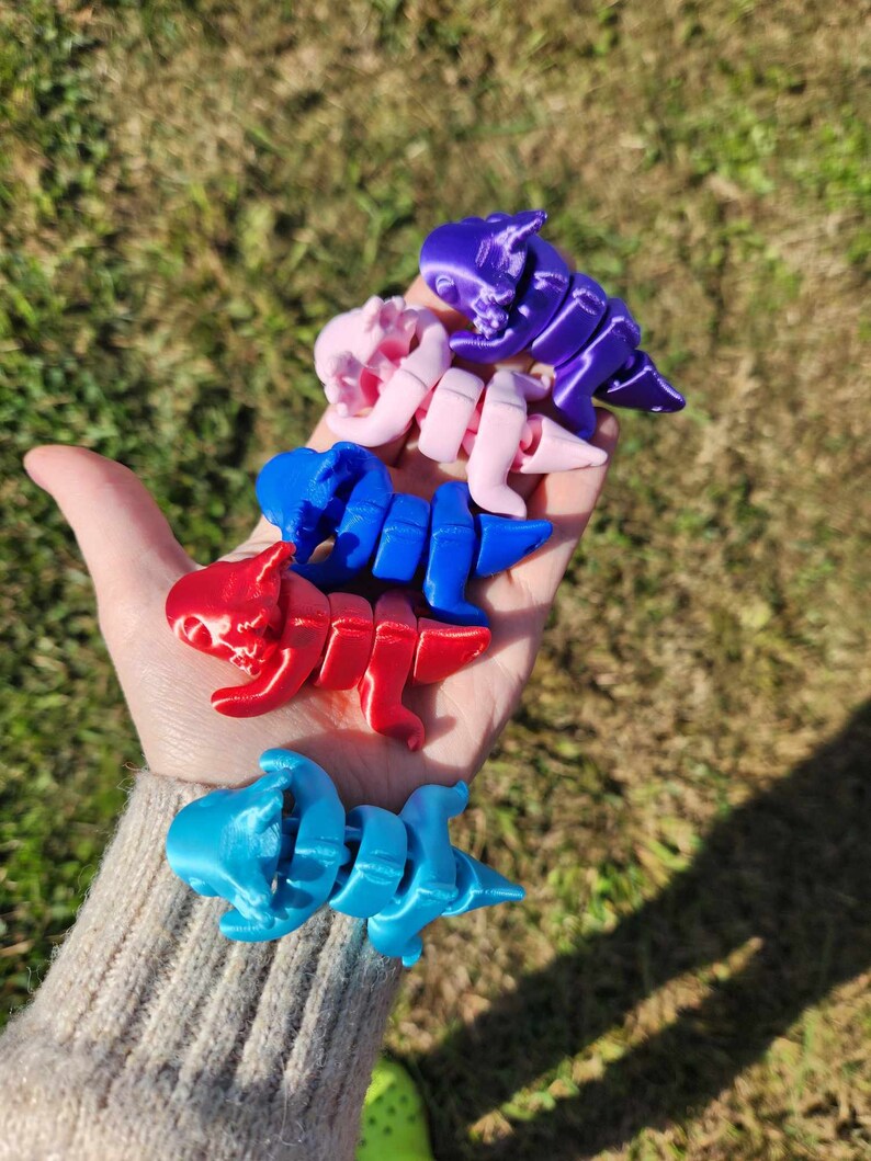 May include: Five small, articulated dinosaur toys in various colors, including blue, red, pink, and purple. The toys are made of plastic and are posed in a variety of positions.