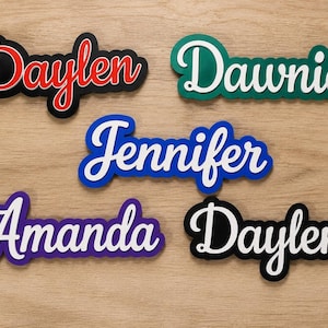May include: Five custom name signs in a cursive script font. The names Daylen, Dawnie, Jennifer, Amanda, and Daylen are displayed in white or red lettering with contrasting coloured backings in black, green, blue, and purple, creating a layered effect.