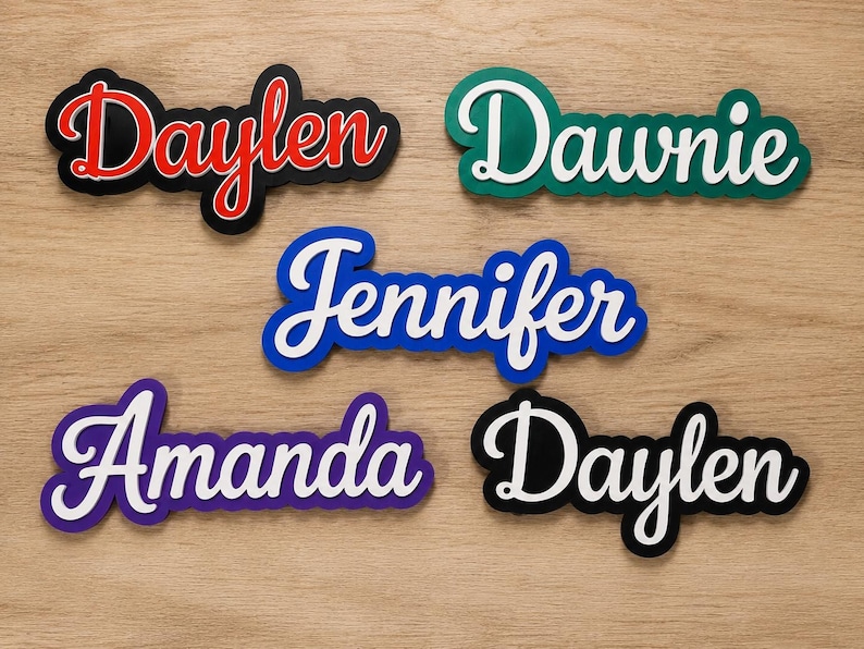 May include: Five custom name signs in a cursive script font. The names Daylen, Dawnie, Jennifer, Amanda, and Daylen are displayed in white or red lettering with contrasting coloured backings in black, green, blue, and purple, creating a layered effect.