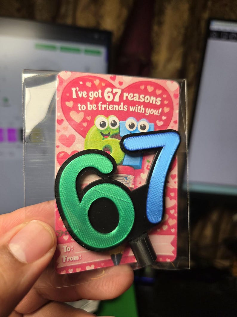May include: A friendship-themed gift tag with the text "I've got 67 reasons to be friends with you!" The tag features a green and blue number "67" design. The background is pink with heart shapes. The tag is in a clear plastic sleeve.
