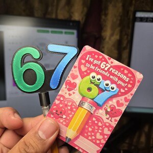 May include: A greeting card with the text "I've got 67 reasons to be friends with you!" features a pencil design with the numbers 6 and 7 as cartoon characters. A separate 3D-printed number 67 is also visible.
