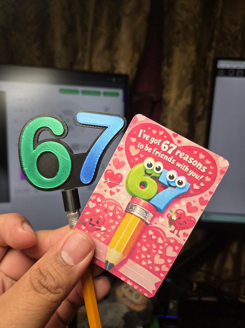 May include: A greeting card with the text "I've got 67 reasons to be friends with you!" features a pencil design with the numbers 6 and 7 as cartoon characters. A separate 3D-printed number 67 is also visible.
