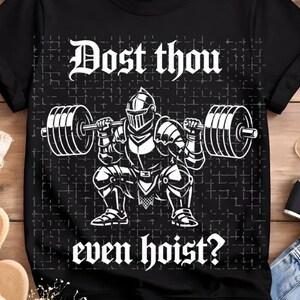May include: Black t-shirt with a white graphic of a knight lifting weights, and the text "Dost thou even hoist?" The design features a knight in full armor squatting with a barbell. The shirt is a classic crew neck.
