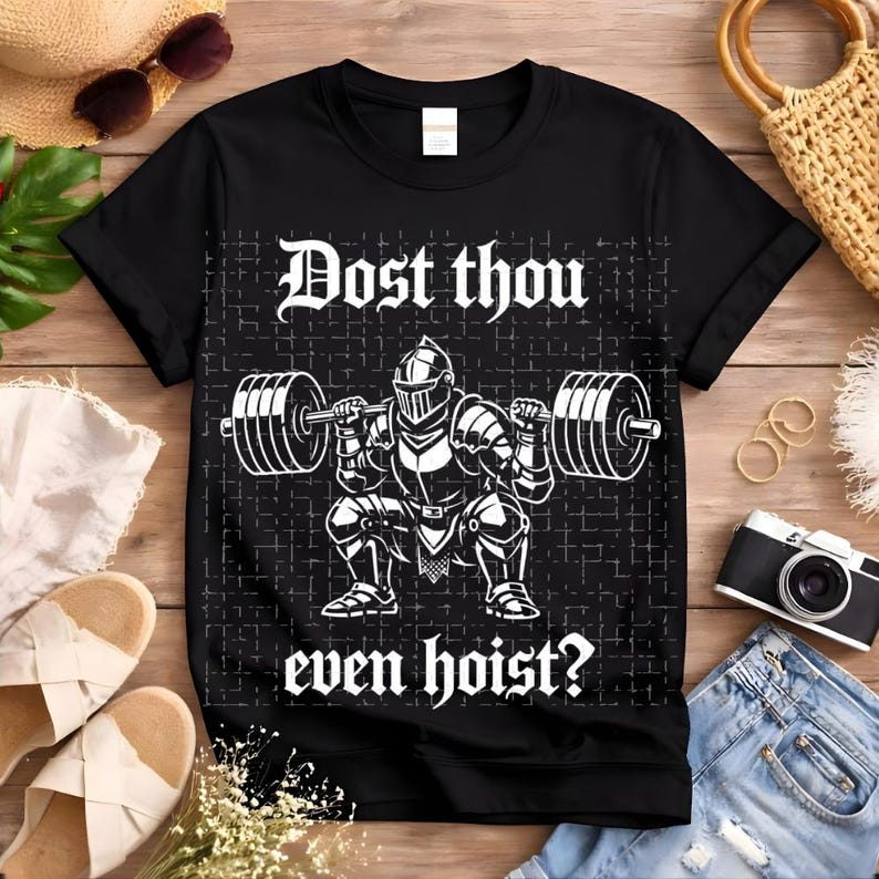 May include: Black t-shirt with a white graphic of a knight lifting weights, and the text "Dost thou even hoist?" The design features a knight in full armor squatting with a barbell. The shirt is a classic crew neck.
