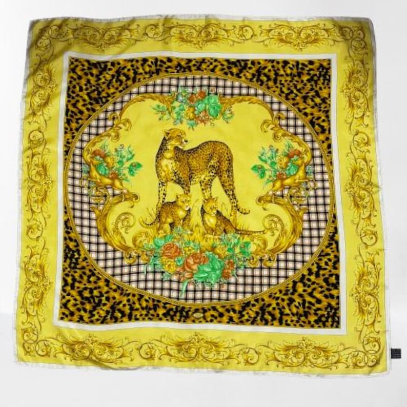 May include: Square yellow scarf with a cheetah family design. The scarf features a cheetah mother and two cubs in a floral and gold frame, set against a black and white checkered background, with a leopard print border.