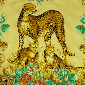 May include: A yellow textile featuring a cheetah and two cubs with a spotted pattern. The cheetahs are surrounded by floral and ornamental designs in shades of green, brown, and gold. The background is a solid yellow.