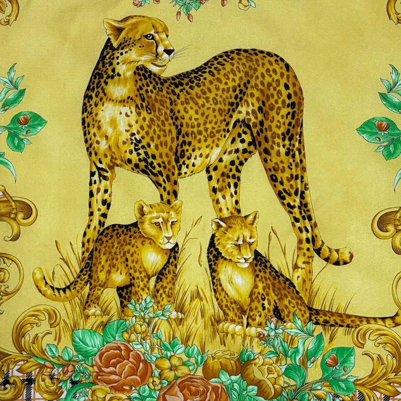 May include: A yellow textile featuring a cheetah and two cubs with a spotted pattern. The cheetahs are surrounded by floral and ornamental designs in shades of green, brown, and gold. The background is a solid yellow.