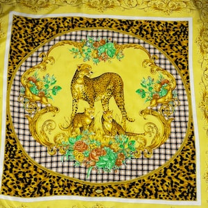 May include: A square yellow scarf with a cheetah family design. The center features a cheetah with two cubs, surrounded by floral and gold scrollwork. The border has a black and white checkered pattern and a leopard print.