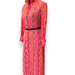 May include: A long-sleeved red dress with a white floral pattern and a black belt. The dress has a button-up front and a collared neckline.