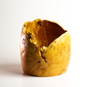 Könnte beinhalten: Eine große, gelbe Holzschale mit einer einzigartigen, natürlichen und organischen Form. Die Schale hat eine raue, strukturierte Oberfläche und eine breite Öffnung.