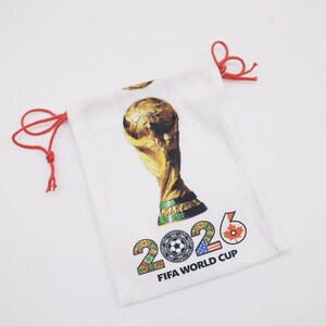 Puede incluir: Bolsa blanca con cordón con un trofeo dorado y el texto "2026 FIFA WORLD CUP". La bolsa tiene cordones rojos y un diseño que incluye un balón de fútbol, la bandera estadounidense y una hoja de arce.