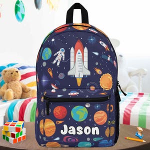 May include: A navy blue backpack featuring a space theme with planets, rockets, and astronauts. The backpack has a front pocket and the name "Jason" printed in white. The design includes various colorful planets and stars.