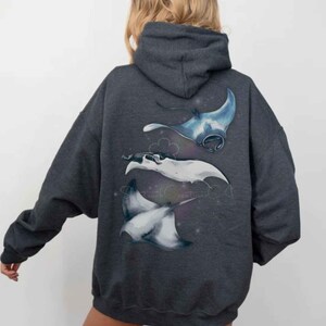 May include: Charcoal grey hoodie with a watercolour illustration of three manta rays in blue and white. The hoodie has a drawstring hood and a relaxed fit. The manta ray design is on the back of the hoodie, ideal for casual wear.