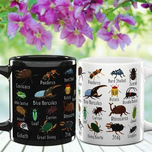 K&ouml;nnte beinhalten: Zwei Keramikbecher, einer schwarz und einer wei&szlig;, jeweils mit farbenfrohen Illustrationen verschiedener Insekten und ihren Namen verziert. Die Becher stehen vor einem Hintergrund aus leuchtenden lila Blumen.