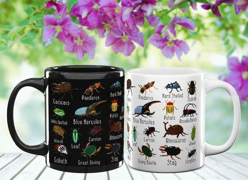 K&ouml;nnte beinhalten: Zwei Keramikbecher, einer schwarz und einer wei&szlig;, jeweils mit farbenfrohen Illustrationen verschiedener Insekten und ihren Namen verziert. Die Becher stehen vor einem Hintergrund aus leuchtenden lila Blumen.