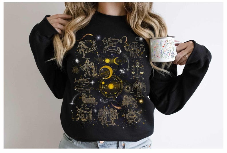 May include: Black sweatshirt with a gold zodiac constellation print on a dark blue background. The constellations include Aries, Taurus, Gemini, Cancer, Leo, Virgo, Libra, Scorpio, Sagittarius, Capricorn, Aquarius, and Pisces.