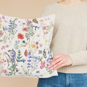 May include: A white pillow with a floral pattern featuring a variety of colorful flowers and butterflies. The pillow is made of a soft, comfortable fabric and is perfect for adding a touch of nature to any room.