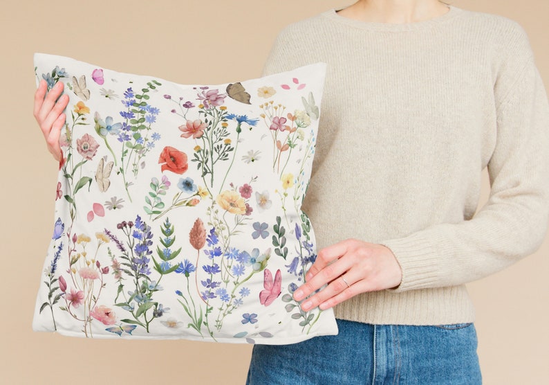 May include: A white pillow with a floral pattern featuring a variety of colorful flowers and butterflies. The pillow is made of a soft, comfortable fabric and is perfect for adding a touch of nature to any room.