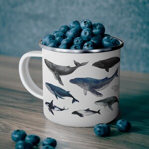 Peut inclure: Une tasse en &eacute;mail blanc avec un motif de baleines bleues et grises. La tasse est remplie de myrtilles.