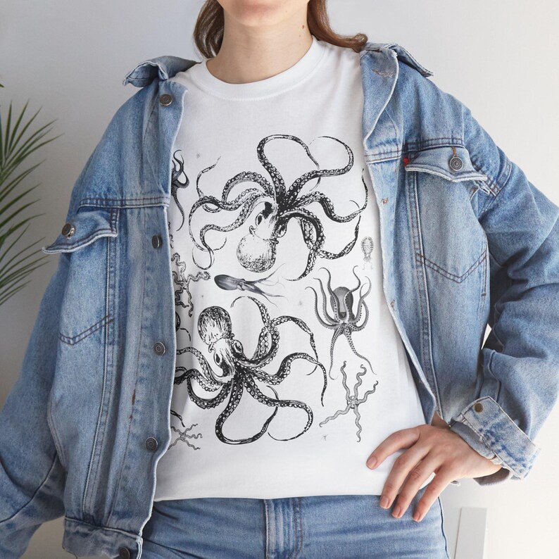 May include: A white t-shirt featuring a detailed black ink illustration of multiple octopuses and sea creatures, worn under a light blue denim jacket. The graphic print displays various marine life forms with intricate tentacles and textures.