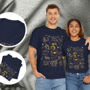 May include: Two navy blue t-shirts with a gold zodiac constellation print. The shirts feature a variety of zodiac signs, including Aries, Taurus, Gemini, Cancer, Leo, Virgo, Libra, Scorpio, Sagittarius, Capricorn, Aquarius, and Pisces.