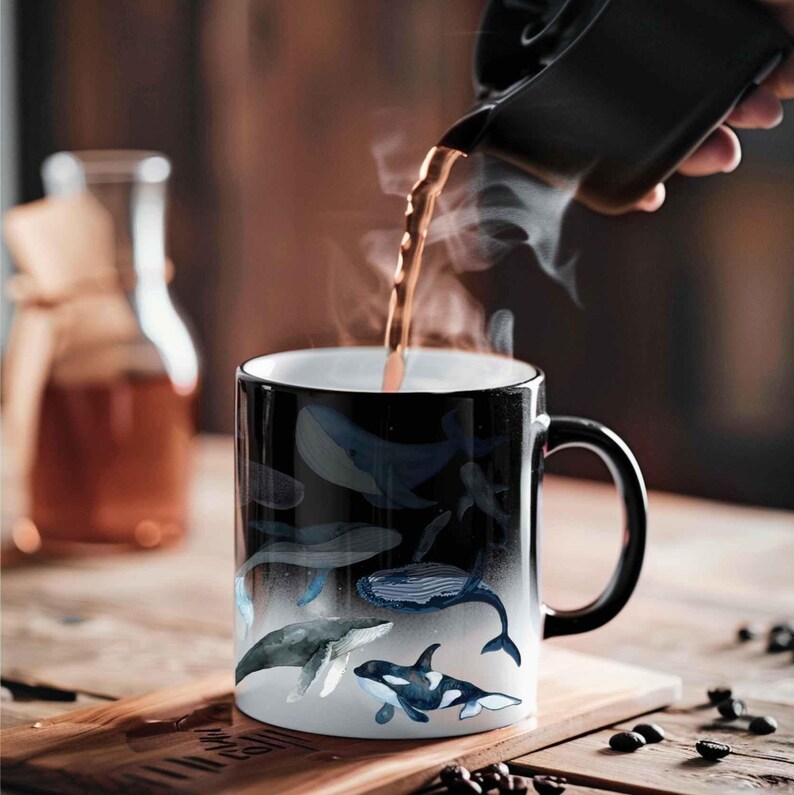 May include: A black ceramic mug with a white interior, featuring a whale design. The mug is being filled with a dark liquid, creating steam. The mug is on a wooden surface.