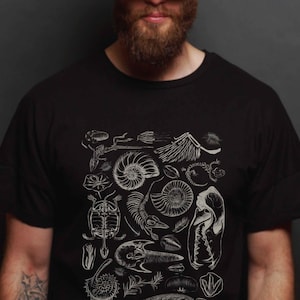 May include: A black short-sleeved t-shirt featuring a white graphic print of various fossils, including ammonites, a turtle skeleton, a bird skull, and other prehistoric biological specimens arranged in a detailed, scientific illustration style.