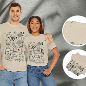 May include: A beige short-sleeve t-shirt featuring a black graphic print of various prehistoric fossils, including ammonites, a turtle, and skeletal remains. The design is centered on the front of the shirt, which has a crew neckline and a standard fit.