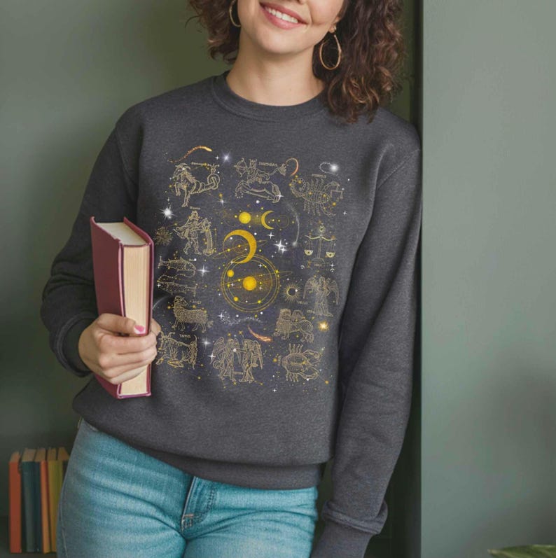 May include: A dark gray sweatshirt with a gold zodiac constellation print. The print features all 12 zodiac signs, the sun, moon, and stars.
