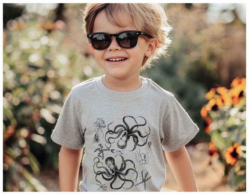 May include: A light gray short-sleeved t-shirt featuring a detailed black ink-style graphic print of multiple octopuses and various sea creatures arranged across the front of the garment, with a crew neckline and a standard fit.