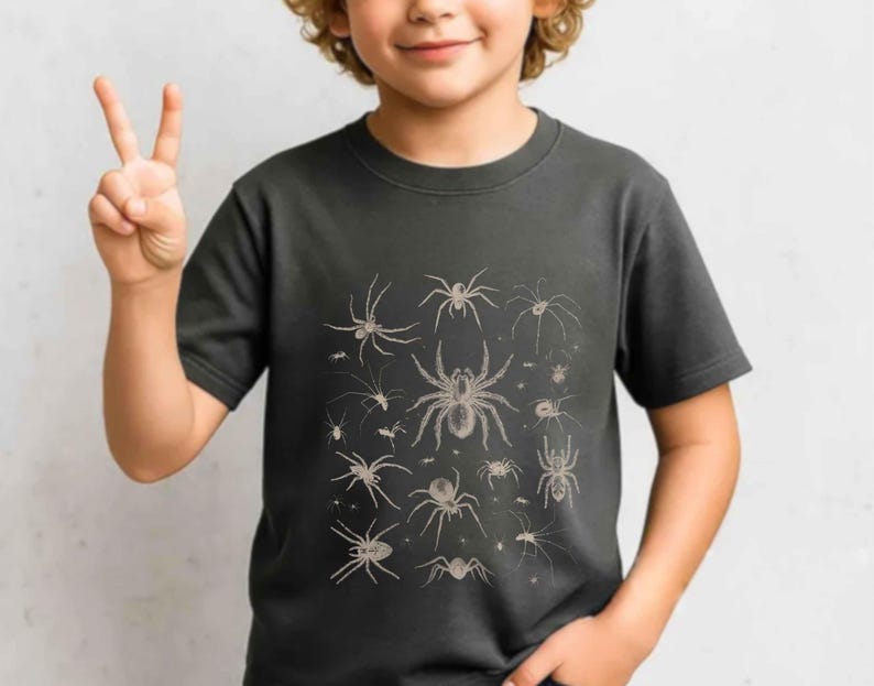 May include: A dark grey short-sleeved t-shirt featuring a detailed, light-coloured graphic print of various spider species arranged in a collection. The design showcases multiple arachnids of different sizes and shapes centred on the chest area.
