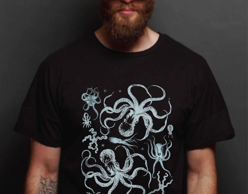 May include: A black short-sleeved t-shirt featuring a detailed, light blue graphic print of various marine creatures, including two large octopuses, a starfish, and other sea life arranged in a cluster across the center of the chest area.