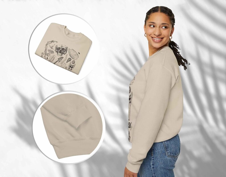 Op de afbeelding: Een beige sweatshirt met lange mouwen en een zwarte grafische print in inktstijl van een schedel, diverse schelpen en botanische elementen op de voorzijde. Het kledingstuk heeft een ronde hals en geribbelde boorden bij de mouwen.