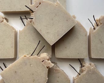 Op de afbeelding: Een close-up van verschillende repen handgemaakte zeep. De zeep is licht beige van kleur en heeft een ruw, getextureerd oppervlak. De repen zijn willekeurig gerangschikt op een wit oppervlak.