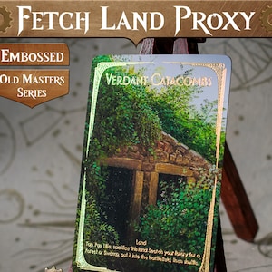 May include: A green and gold foil card with the text "VERDANT CATACOMBS" and "Land" printed on it. The card features a photo of a stone building with a green overgrown roof and a forest background.