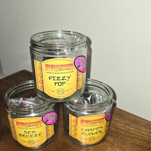 May include: Three glass jars of incense with yellow and black labels. The labels read "Wildberry", "Fizzy Pop", "Sea Breeze", and "Champa Flower". Each jar has a pink sticker that says "Backflow Cones".